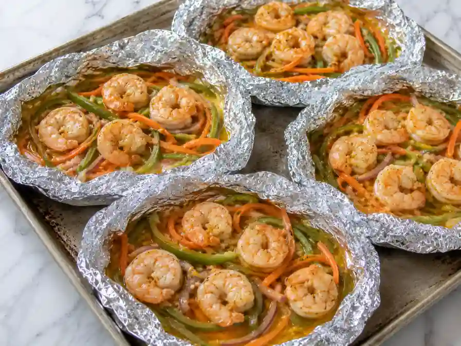 Cooked shrimp and vegetables in open foil packets before adding cheese