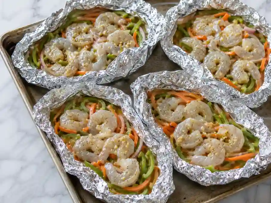 Raw shrimp arranged over vegetables in open foil packets