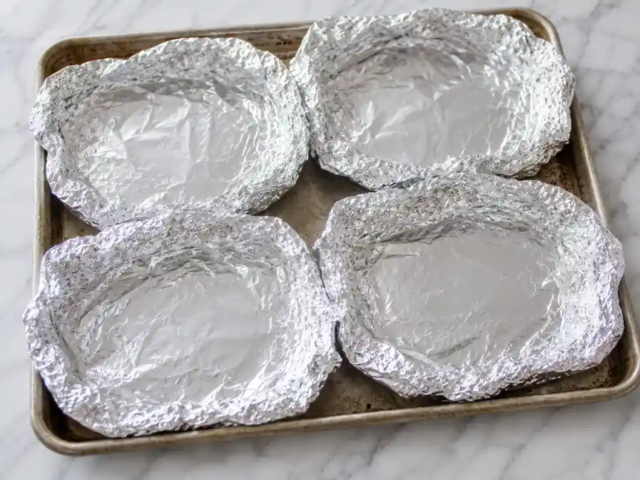 Shrimp foil packets prepared with four empty aluminum foil sheets on a rimmed baking tray